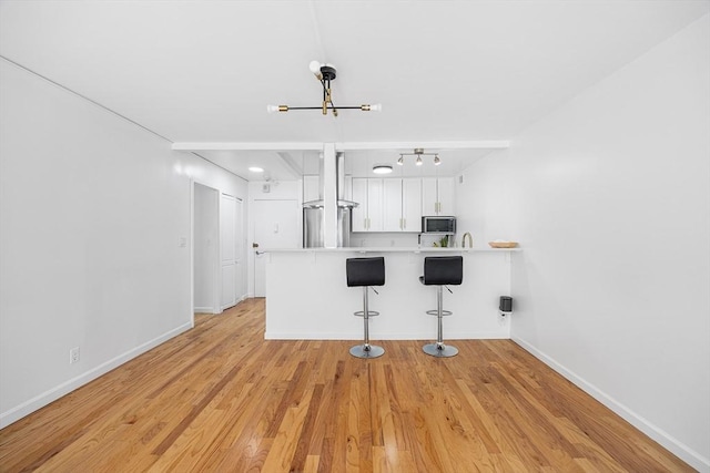 99 Pond Ave Unit 202, Brookline, MA 02445 - kitchen featuring stainless steel microwave, white cabinetry, a peninsula, a kitchen bar, and light countertops