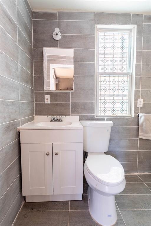 bathroom featuring vanity, tile patterned flooring, toilet, and tile walls