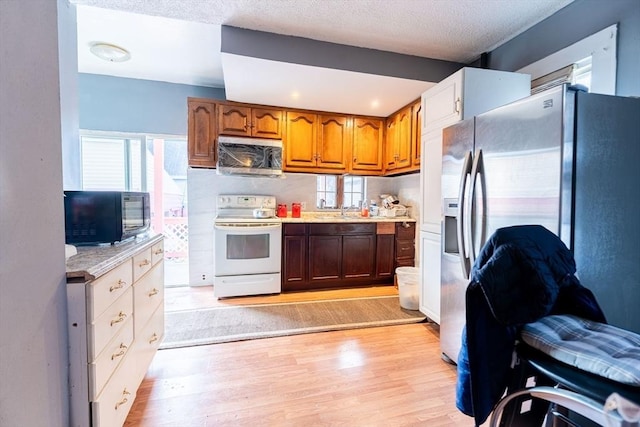 kitchen featuring sink, a textured ceiling, light wood-type flooring, stainless steel fridge, and electric stove