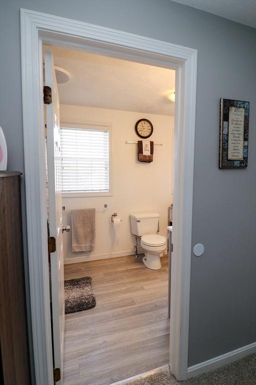 bathroom with toilet, baseboards, and wood finished floors