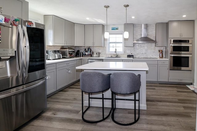 kitchen featuring a kitchen bar, wall chimney exhaust hood, stainless steel appliances, gray cabinetry, and decorative backsplash