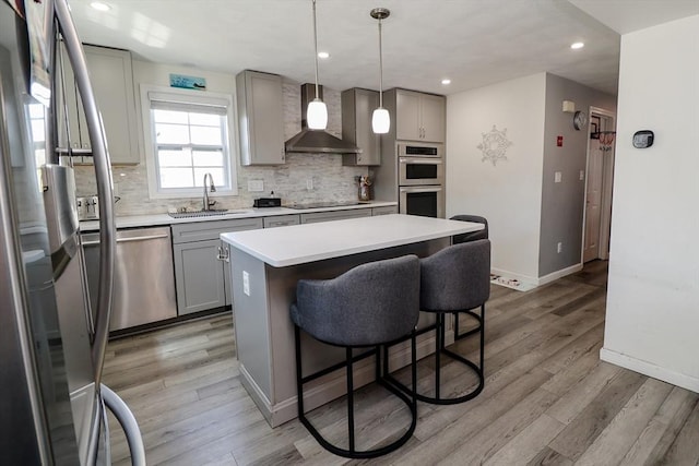 kitchen with gray cabinetry, wall chimney exhaust hood, appliances with stainless steel finishes, and a sink
