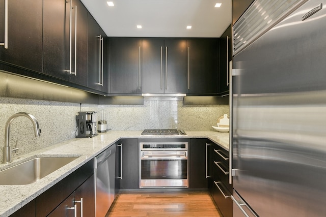 kitchen featuring light stone counters, backsplash, appliances with stainless steel finishes, sink, and light hardwood / wood-style floors