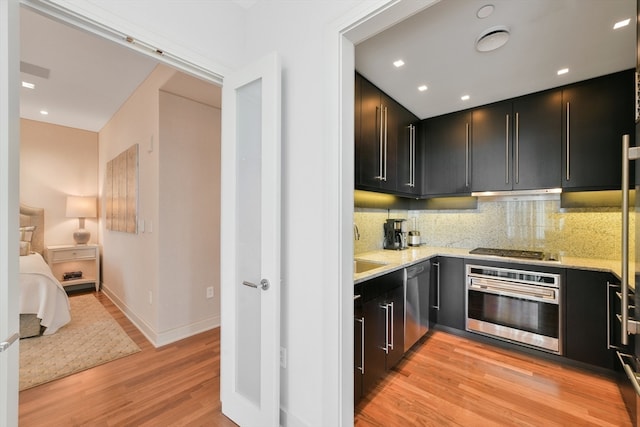 kitchen featuring light wood-type flooring, decorative backsplash, light stone counters, and stainless steel appliances