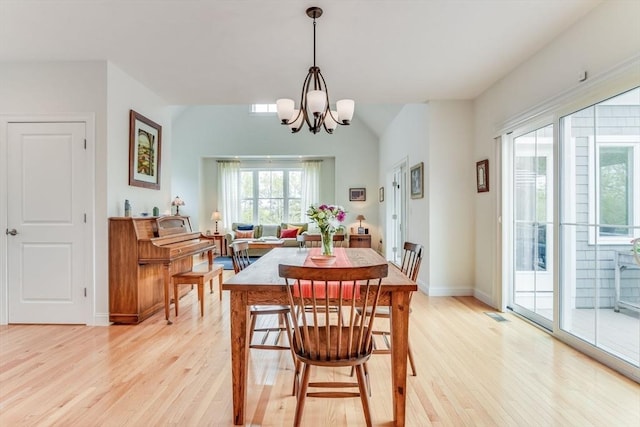 dining area featuring light wood-style flooring, visible vents, baseboards, vaulted ceiling, and an inviting chandelier