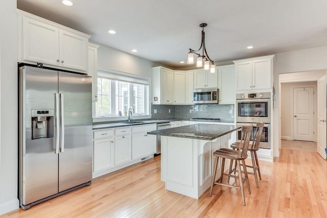 kitchen with backsplash, light wood-style flooring, appliances with stainless steel finishes, a sink, and a kitchen breakfast bar