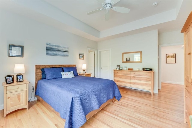 bedroom with ceiling fan, light wood-style flooring, baseboards, and a raised ceiling