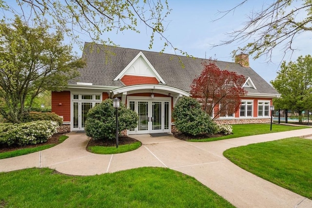 view of front of house featuring stone siding, a chimney, roof with shingles, french doors, and a front yard