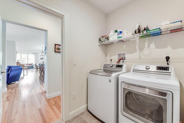 laundry area with laundry area, light wood finished floors, baseboards, separate washer and dryer, and a notable chandelier