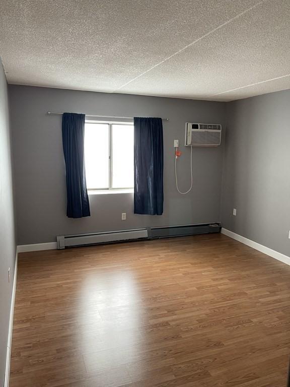 empty room with a wall mounted air conditioner, wood-type flooring, a textured ceiling, and a baseboard radiator