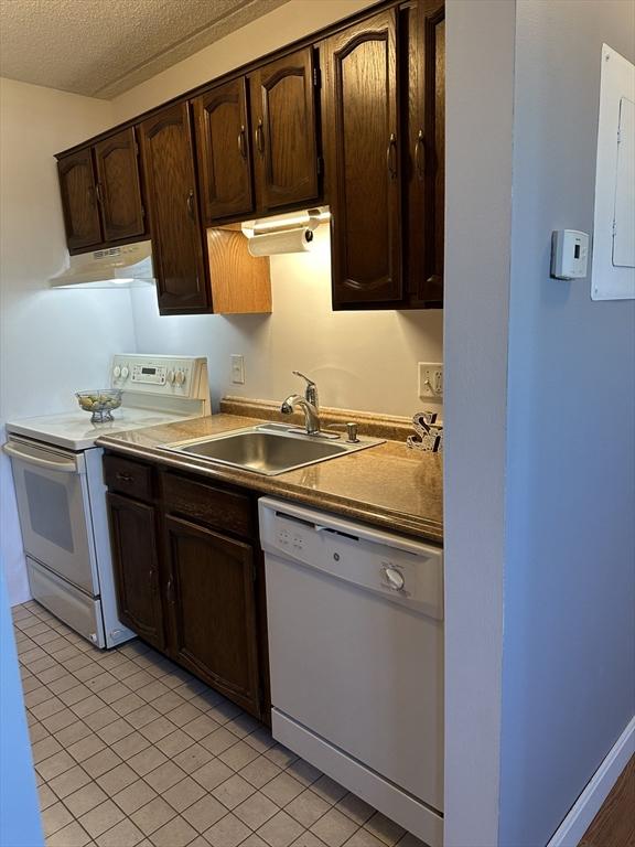 kitchen with white appliances, sink, a textured ceiling, light tile patterned flooring, and dark brown cabinetry