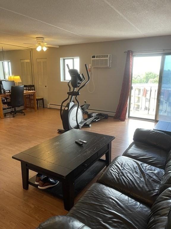 living room featuring ceiling fan, a baseboard radiator, a wall unit AC, wood-type flooring, and a textured ceiling