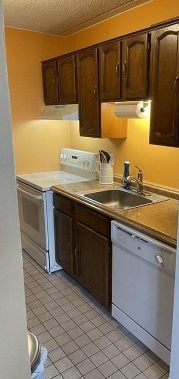 kitchen featuring dark brown cabinetry, sink, light tile patterned floors, and white appliances