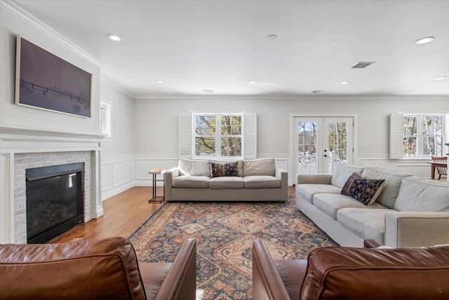 living area with visible vents, ornamental molding, french doors, light wood-type flooring, and a brick fireplace