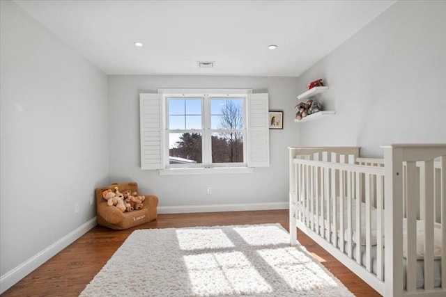 bedroom featuring recessed lighting, wood finished floors, visible vents, baseboards, and a nursery area