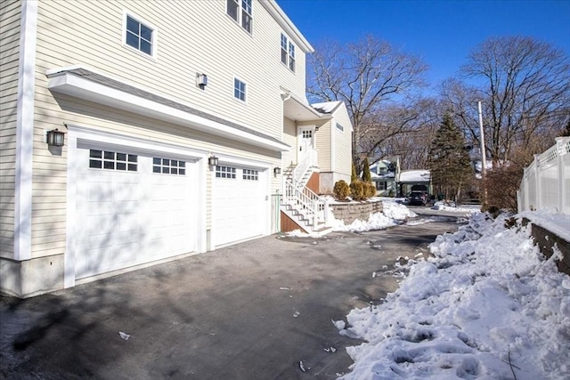 view of snow covered exterior featuring driveway, stairway, and an attached garage