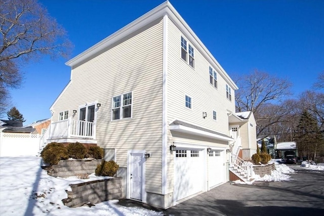 snow covered property with a garage, fence, and aphalt driveway