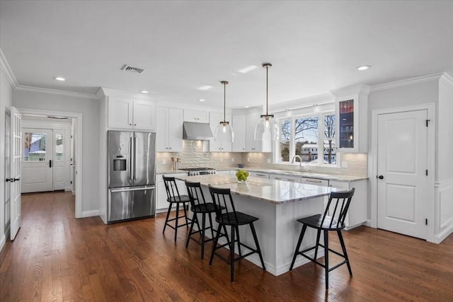 kitchen with decorative light fixtures, glass insert cabinets, a kitchen island, under cabinet range hood, and stainless steel fridge with ice dispenser