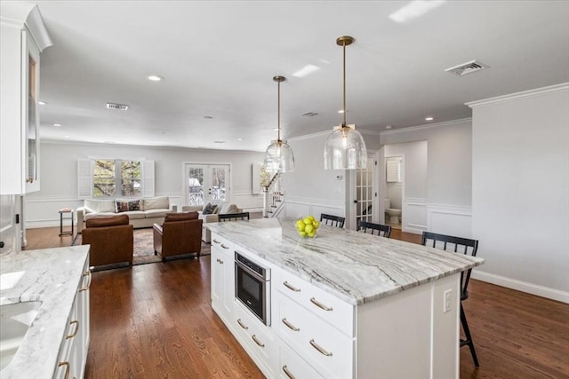 kitchen with a kitchen island, stainless steel microwave, a breakfast bar, open floor plan, and white cabinetry