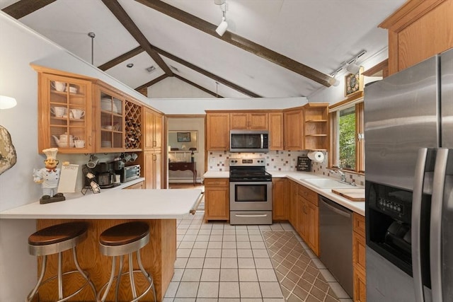 kitchen with a sink, a peninsula, lofted ceiling with beams, tasteful backsplash, and appliances with stainless steel finishes