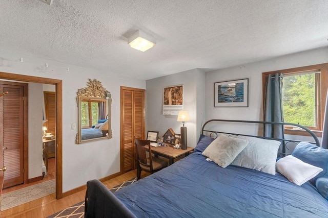 bedroom featuring a closet, a textured ceiling, light wood-style flooring, and baseboards