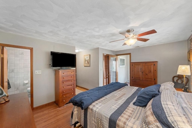 bedroom with baseboards, a baseboard heating unit, ensuite bathroom, ceiling fan, and light wood-type flooring