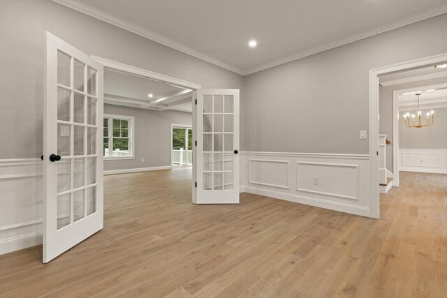 spare room featuring an inviting chandelier, light hardwood / wood-style floors, a raised ceiling, and crown molding