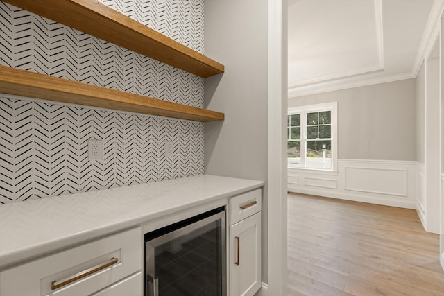 kitchen with light hardwood / wood-style flooring, beverage cooler, white cabinetry, and crown molding