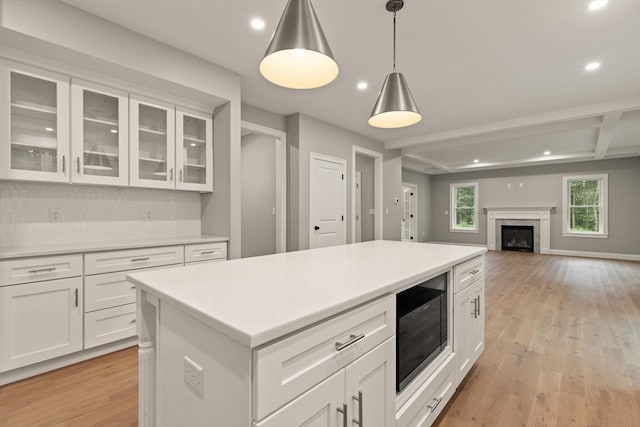 kitchen with white cabinets, black microwave, a high end fireplace, pendant lighting, and light wood-type flooring