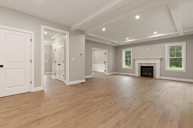 unfurnished living room with light hardwood / wood-style flooring, a premium fireplace, and beam ceiling