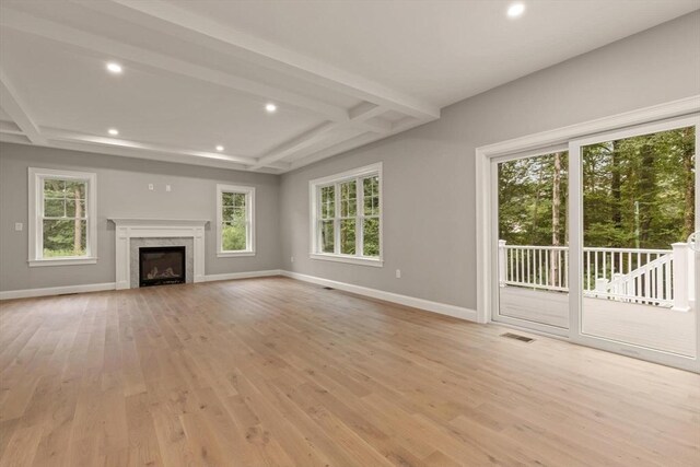 unfurnished living room with light hardwood / wood-style floors, beamed ceiling, and a premium fireplace