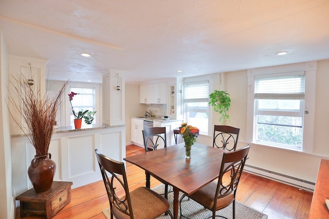 dining space with baseboard heating, sink, and light wood-type flooring