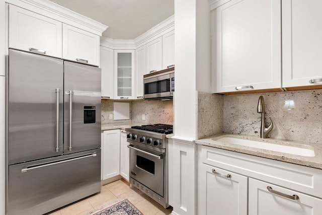 kitchen with white cabinetry, sink, light stone counters, and premium appliances