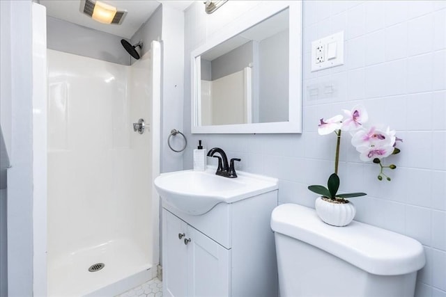 bathroom featuring vanity, toilet, a shower, and tile walls