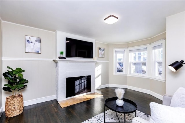 living room featuring dark hardwood / wood-style flooring, ornamental molding, and a brick fireplace