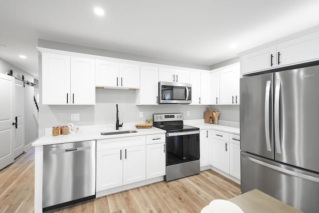 kitchen featuring white cabinetry, appliances with stainless steel finishes, a barn door, and sink