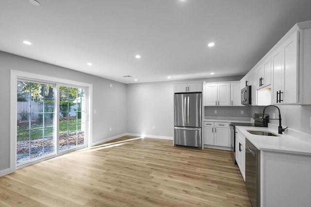 kitchen featuring appliances with stainless steel finishes, white cabinetry, sink, light stone counters, and light hardwood / wood-style floors