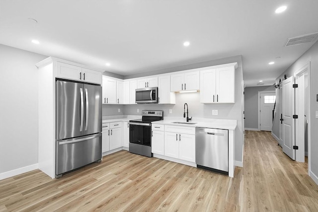 kitchen with sink, white cabinetry, stainless steel appliances, light hardwood / wood-style floors, and a barn door