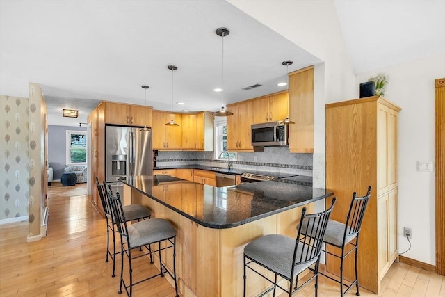 kitchen with a sink, light wood finished floors, stainless steel appliances, baseboards, and a peninsula