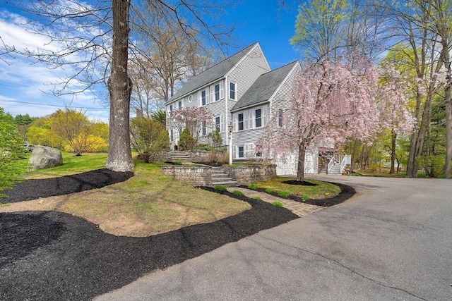 view of property exterior featuring an attached garage, driveway, a shingled roof, and stairs