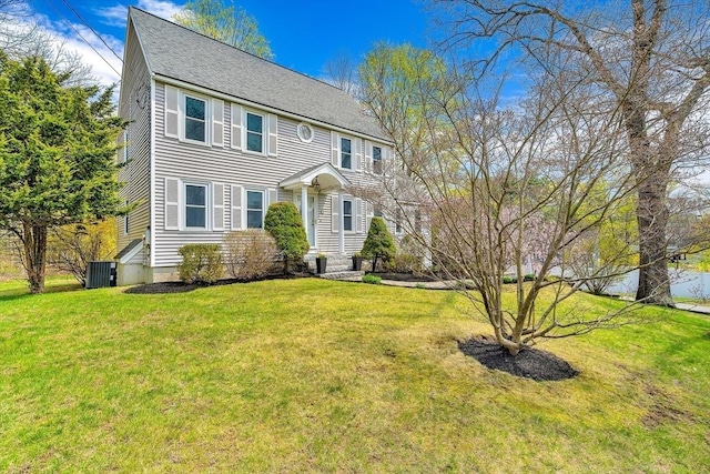 colonial house with central AC unit, roof with shingles, and a front yard