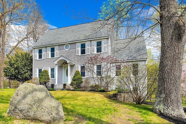 colonial inspired home featuring roof with shingles and a front yard