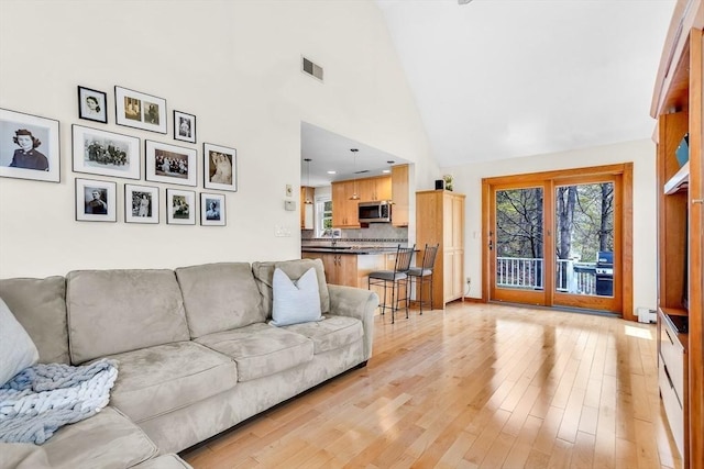 living area featuring high vaulted ceiling, a baseboard heating unit, light wood-type flooring, and visible vents