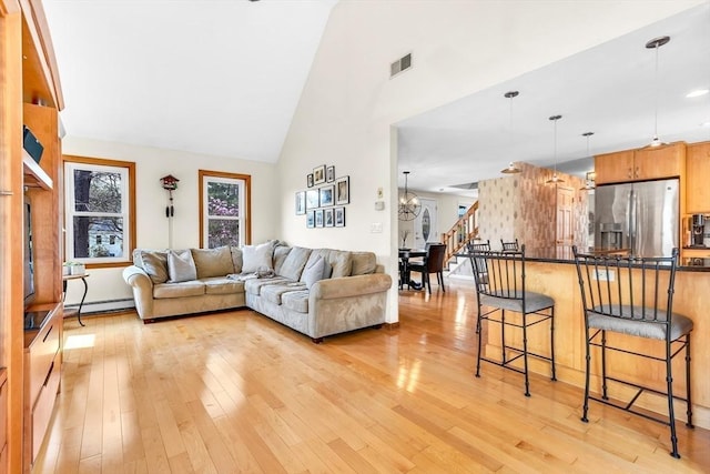 living area featuring high vaulted ceiling, baseboard heating, light wood finished floors, and visible vents