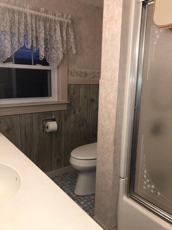 full bathroom featuring vanity, tile patterned floors, wooden walls, toilet, and enclosed tub / shower combo