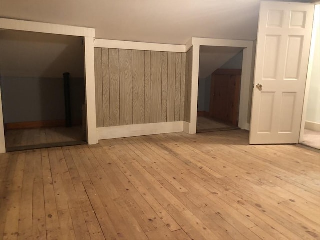 bonus room with vaulted ceiling, light hardwood / wood-style flooring, and wood walls