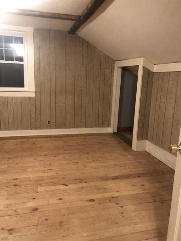 bonus room featuring light wood-type flooring, vaulted ceiling with beams, and wooden walls