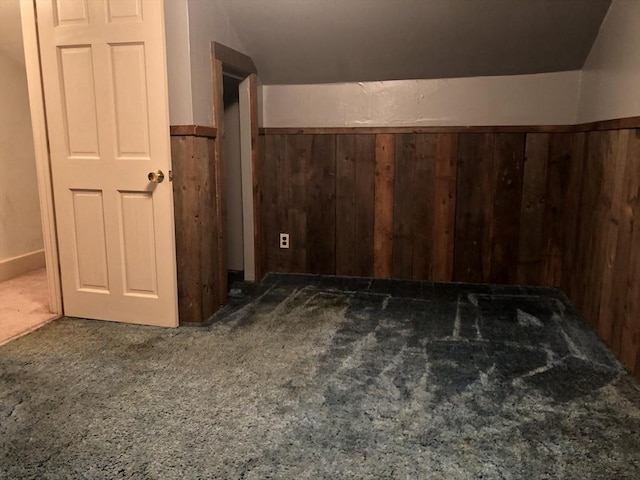 bonus room featuring wood walls, dark carpet, and vaulted ceiling