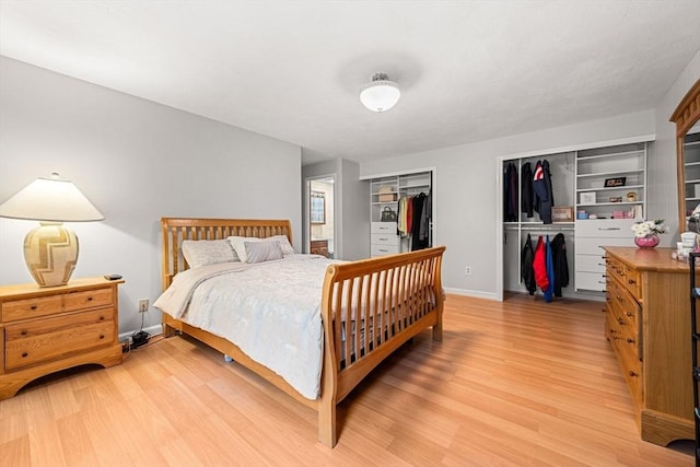 bedroom featuring light wood finished floors, baseboards, and two closets