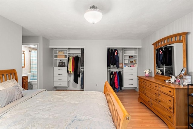 bedroom with two closets, light wood-type flooring, and ensuite bathroom
